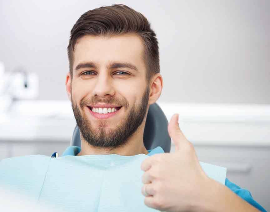 Smiling man in dentist’s chair giving thumbs up