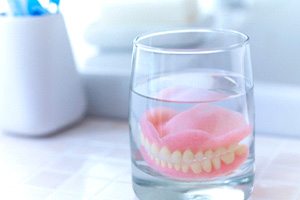 A closeup of dentures soaking in a glass of solution
