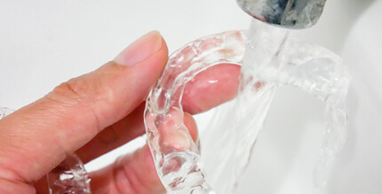 Patient rinsing clear aligner in sink 