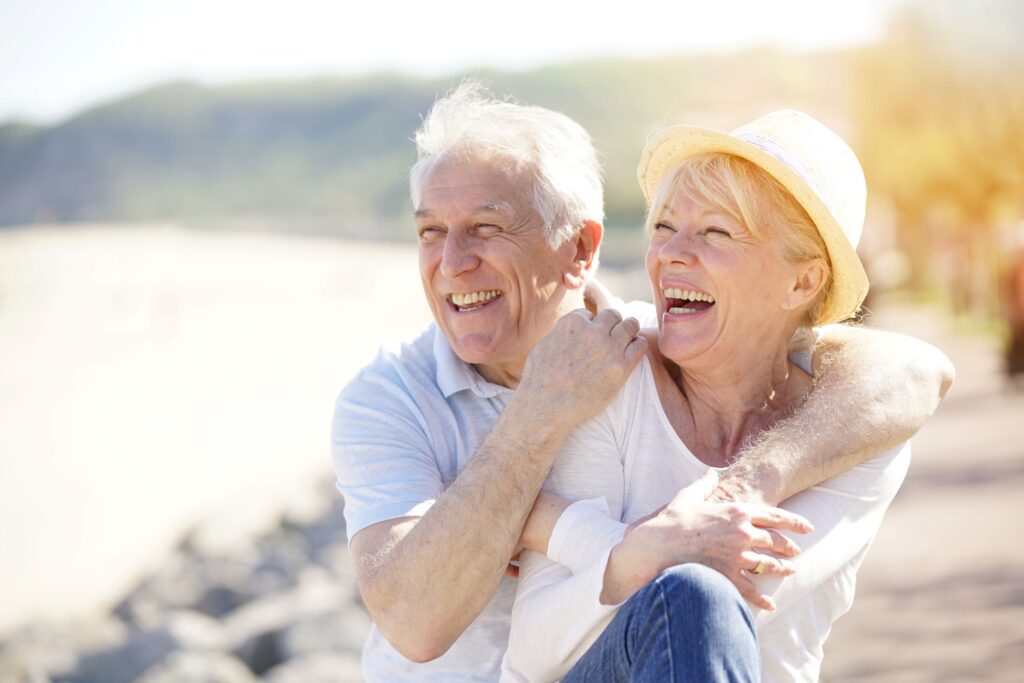 Man in t-shirt hugging woman in straw hat outside by the shore